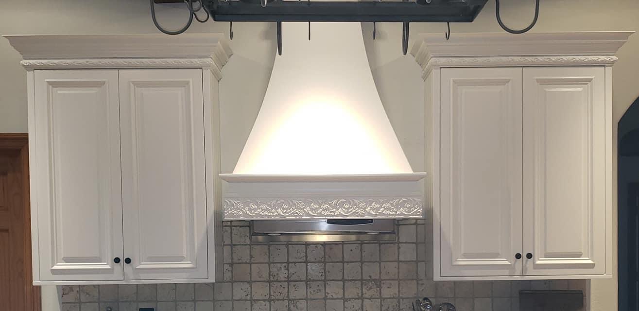 Close-up of white painted upper cabinets and a decorative range hood surround